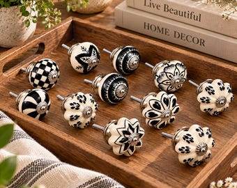 Peut inclure: Un ensemble de douze boutons de placard en céramique ronde présentant divers motifs noirs et blancs, notamment des designs à carreaux, floraux, rayés et en forme d'étoile. Chaque bouton possède une base en métal argenté et une vis centrale.