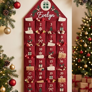 May include: A deep red fabric advent calendar shaped like a house, featuring the name Evelyn in white script, a gift icon, and twenty-four numbered pockets. Each pocket displays white holiday graphics like snowflakes, trees, and holly, with various small items tucked inside.
