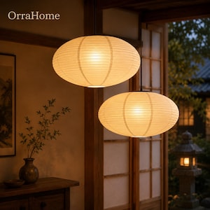 May include: Two oval-shaped pendant lamps with ribbed white paper shades suspended from the ceiling. The lamps emit a warm, soft glow, illuminating the space. The text OrraHome is visible in the upper left corner of the image.