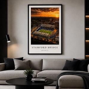 May include: A framed wall art print featuring an aerial view of Stamford Bridge stadium at sunset. The image shows the green pitch and surrounding city skyline under an orange sky. The text reads STAMFORD BRIDGE and CHELSEA FC below.