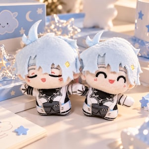 May include: Two plush dolls with light blue hair and white and black outfits. One doll has closed eyes, and the other has a wide, smiling expression. Both feature small yellow diamond accents on their hair and detailed printed clothing designs.