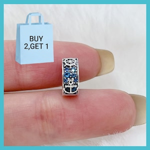 May include: A silver charm bead featuring a nautical theme with a ship wheel at the top and an anchor at the bottom, accented with small blue crystals. The charm includes a graphic of a light blue shopping bag with the text BUY 2, GET 1.