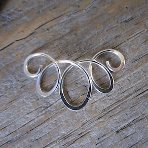 May include: A silver swirl design pendant with a delicate and intricate pattern. The pendant is made of smooth, polished metal and has a modern, minimalist aesthetic.