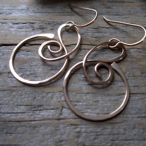 May include: A pair of gold-toned earrings with a swirl design. The earrings are made of wire and have a hammered finish.