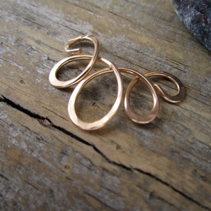 May include: A gold-toned ear cuff with a delicate, flowing design. The cuff is made of multiple loops and curves, creating a unique and intricate look.