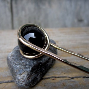 May include: A gold hair stick with a black onyx bead. The bead is wrapped in gold wire.