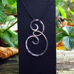 May include: A silver pendant necklace with a double spiral design on a black display card. The pendant is made of two intertwined spirals, one larger than the other.