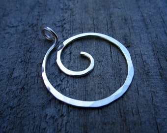 Puede incluir: Un colgante de plata con un acabado martillado en forma de espiral. El colgante está diseñado para ser usado en un collar.