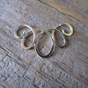 May include: A silver metal pendant with a swirling, abstract design. The pendant is made of smooth, polished metal and has a delicate, intricate shape.