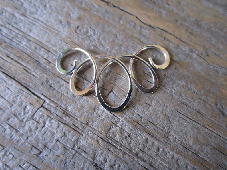 May include: A silver metal pendant with a swirling, abstract design. The pendant is made of smooth, polished metal and has a delicate, intricate shape.
