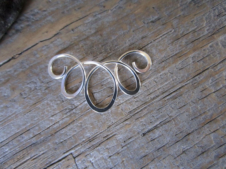 May include: A silver swirl design pendant with a delicate and intricate pattern. The pendant is made of smooth, polished metal and has a modern, minimalist aesthetic.