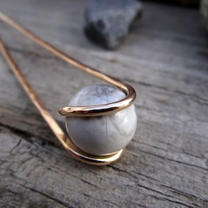 May include: A gold-toned hair stick with a white marble sphere at the end. The sphere is wrapped in a gold-toned wire.