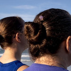 May include: Two people with brown hair, both wearing blue shirts, stand side by side looking out at the ocean.