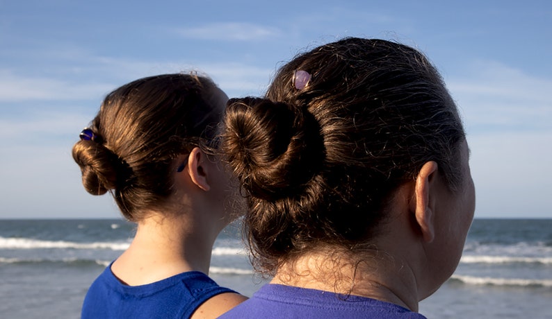 May include: Two people with brown hair, both wearing blue shirts, stand side by side looking out at the ocean.