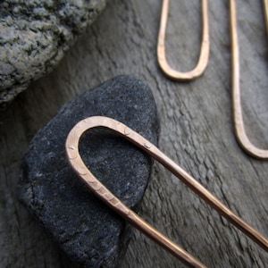 May include: Two copper hair pins with a hammered finish. The pins are U-shaped at the top and straight at the bottom.