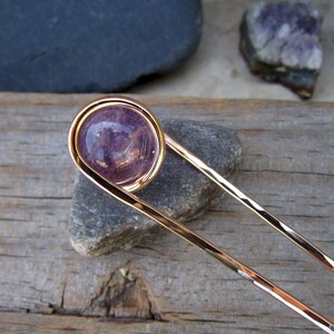 May include: A gold hair stick with a purple amethyst stone set in a wire loop at the top.