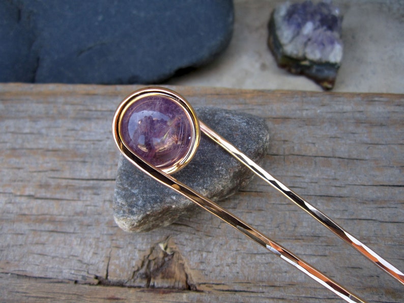 May include: A gold hair stick with a purple amethyst stone set in a wire loop at the top.