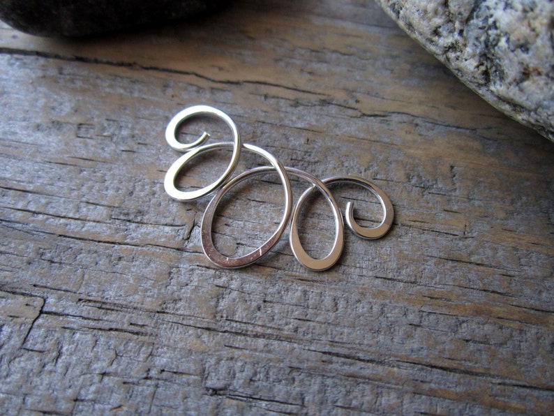 May include: Silver ear cuff with a delicate, swirling design. The cuff is made of a single piece of metal that is bent into a series of loops and curves.