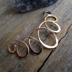 May include: Gold ear cuff with a curved design featuring multiple interconnected loops. The cuff is made of a smooth, shiny metal.