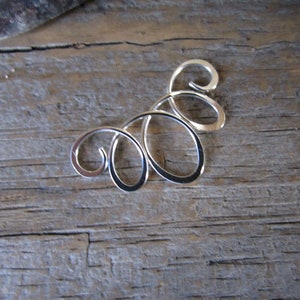 May include: Silver pendant with a swirling, abstract design. The pendant is made of metal and has a smooth, polished finish.