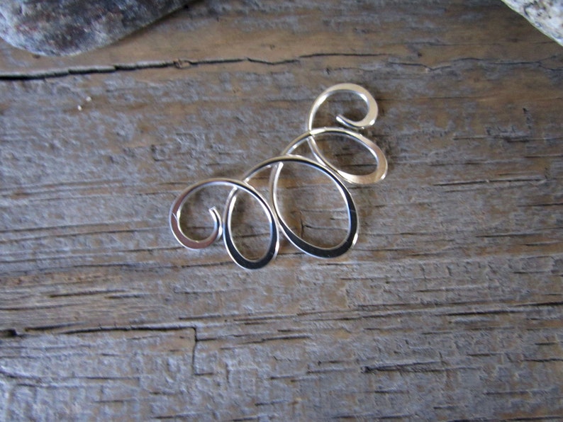 May include: Silver pendant with a swirling, abstract design. The pendant is made of metal and has a smooth, polished finish.