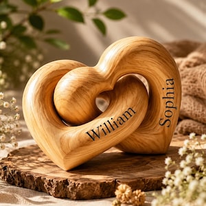 May include: A light brown wooden sculpture featuring two interlocking heart shapes. The smooth, polished wood grain is visible throughout the piece. The name William is engraved on the left heart, and the name Sophia is engraved on the right heart.