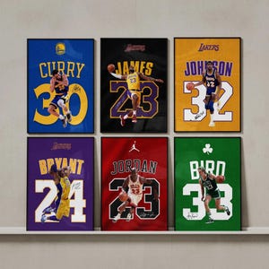 May include: A set of six framed basketball posters featuring professional players Curry, James, Johnson, Bryant, Jordan, and Bird. Each poster displays the player's name, jersey number, team colors, and a signature graphic against a textured background.