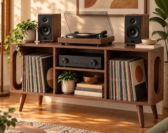 May include: A dark wood media console with tapered legs and oval side cutouts. The top holds a turntable and two speakers. The interior shelves contain two rows of vinyl records, a black audio receiver, a small potted plant, and a wooden bowl.
