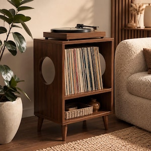 May include: A dark wood record player stand featuring a top surface for a turntable, a middle shelf filled with vinyl records, and a bottom shelf containing a woven basket. The unit has circular cutouts on the sides and four tapered legs.