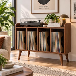 Könnte beinhalten: Ein Schallplatten-Aufbewahrungsmöbel aus Walnussholz mit vier offenen Fächern, die mit Schallplatten gefüllt sind. Oben steht ein schwarzer Plattenspieler neben einer kleinen Messinglampe und zwei Büchern mit den Titeln The Kinfolk Home und A Life More Music.
