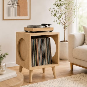 May include: A light wood record player stand with four tapered legs and circular cutouts on the sides. The open central compartment is filled with a collection of vinyl records, and a black turntable sits on the flat top surface of the unit.