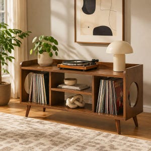 May include: A brown wooden media console with four tapered legs and circular side cutouts. The top surface holds a black record player and a cream-colored mushroom-shaped lamp. The shelves contain rows of vinyl records and a decorative knot object.