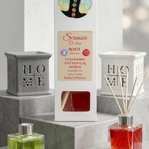 May include: A reed diffuser set featuring a tall white box labelled Serensia Chakras Root with cedarwood, patchouli, and myrrh essential oils. Includes two square glass bottles with green and red liquid, two ceramic HOME holders, and a stack of cards.