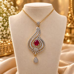 Peut inclure: Un collier à chaîne dorée avec un grand pendentif en forme de goutte. Le pendentif est incrusté de nombreuses petites pierres claires, taillées en baguette et en rond, entourant une pierre rouge vive en forme de poire avec une breloque.