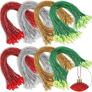 Puede incluir: Una colección de cordones metálicos para colgar en rojo, plata, oro y verde, cada uno con un cierre de plástico a presión en el extremo. Un pequeño recuadro circular muestra un adorno rojo sujeto a uno de los cordones rojos por su anilla.