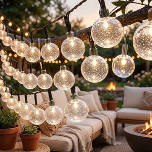 Peut inclure: Une guirlande lumineuse composée de globes sphériques transparents avec une texture interne mouchetée ou à bulles. Chaque ampoule émet une lueur chaude et est suspendue à un cordon sombre. Les lumières sont disposées en plusieurs rangées.