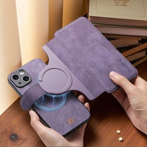 Könnte beinhalten: Eine violette Handyhülle mit strukturierter Oberfläche und einem magnetischen Klappständer auf der Rückseite. Die Hülle zeigt den eingeprägten Schriftzug CaseNeo auf der Lasche und die Initialen RS in Orange auf dem unteren Teil der Handyhülle.