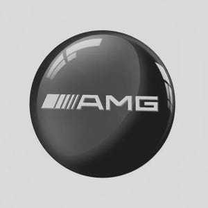 Può includere: Un emblema circolare nero lucido con il testo color argento AMG. Il design include un elemento grafico stilizzato a sinistra delle lettere, con una superficie liscia e riflettente che mostra riflessi di luce sulla parte superiore e laterale.