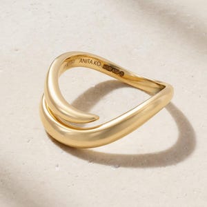 Puede incluir: Un anillo de oro con un diseño liso, curvo y abierto. El interior de la banda está grabado con el texto ANITA KO y el sello 18K 750. El anillo presenta un acabado pulido y una forma fluida y continua que se superpone ligeramente en un extremo.