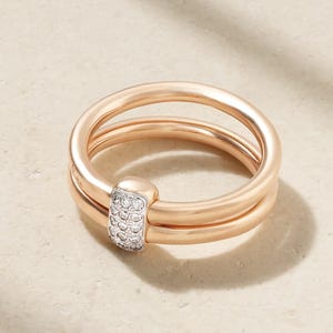 May include: A rose gold double band ring featuring a rectangular silver-toned connector piece set with twelve small, clear, round-cut stones. The two smooth, polished rose gold bands are joined together by the stone-encrusted centre element.