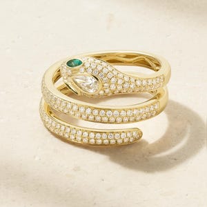 May include: A gold wrap-around ring shaped like a coiled snake. The body is encrusted with numerous small white pavé diamonds. The snake head features a pear-shaped white diamond and a small green gemstone eye, set in polished yellow gold.