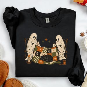 Moletom de Halloween com estampa de fantasmas costurando uma colcha de retalhos com um gato preto, modelo retrô com gola redonda.