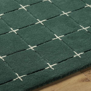 Puede incluir: Una alfombra de color verde bosque profundo con un patrón de cuadrícula repetitivo de líneas blancas finas. La alfombra tiene una textura de pelo denso y copetudo que crea una superficie suave. El diseño de cuadrícula forma cuadrados.