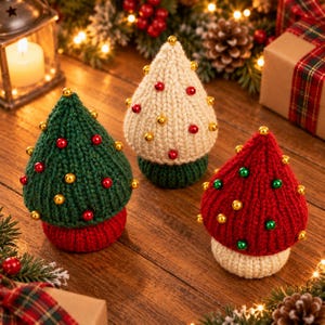 Könnte beinhalten: Drei kegelförmige Strickornamente bestehend aus einem grünen Baum mit roten und goldenen Perlen, einem cremefarbenen Baum mit roten und goldenen Perlen sowie einem roten Baum mit grünen und goldenen Perlen, jeweils mit einer kontrastierenden Basis.