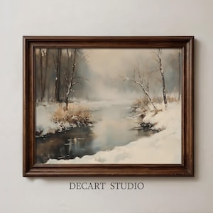 May include: A framed landscape painting depicting a snow-covered riverbank with bare trees and dry grasses under a misty sky. The artwork is enclosed in a dark brown wooden frame. The text DECART STUDIO is printed in black below the frame.