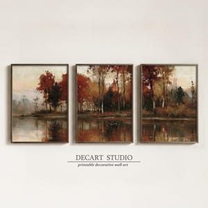 May include: A triptych of framed wall art prints featuring a landscape of autumn trees in shades of red, orange, and brown reflected in a calm lake. The text DECART STUDIO printable decorative wall art is centred below the three framed images.