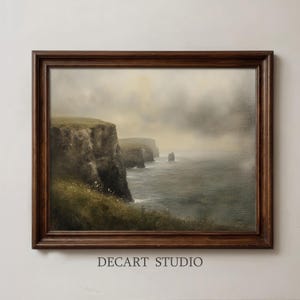 Puede incluir: Una pintura de paisaje enmarcada que representa acantilados costeros oscuros y escarpados sobre un océano gris y brumoso bajo un cielo nublado. La obra está en un marco de madera marrón oscuro, con el texto DECART STUDIO impreso debajo.