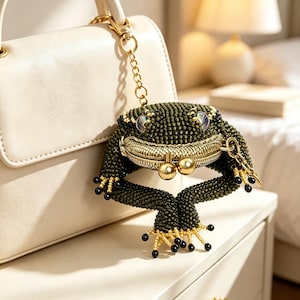 May include: A frog-shaped coin purse crafted from dark green beads with a gold-toned metal kiss-lock clasp. The purse features iridescent eyes, gold-beaded toes with black tips, and a gold chain attachment for securing to a handbag or accessory.
