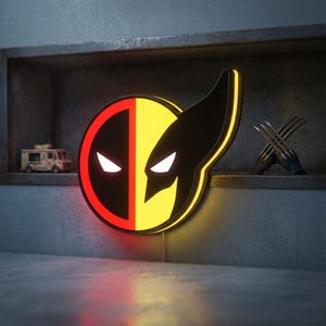 Pode incluir: Um letreiro LED circular de parede com um design dividido, apresentando uma máscara de Deadpool vermelha e preta à esquerda e uma máscara de Wolverine amarela e preta à direita. O letreiro emite um brilho intenso, destacando os olhos angulares.