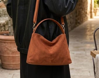 May include: A brown handbag with a smooth, matte texture, featuring a rounded top handle and a long, adjustable shoulder strap. The bag has a structured base and a soft, curved silhouette, presented in a solid, earthy brown color tone.